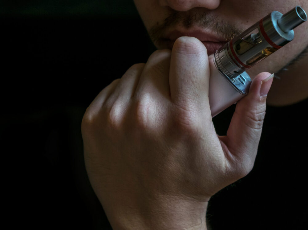 Man with concealed identity smoking a controversial vaping an el Man with concealed identity smoking a controversial vaping an electronic cigarette. Vaping is debatable in the health community if it is safe or a health risk