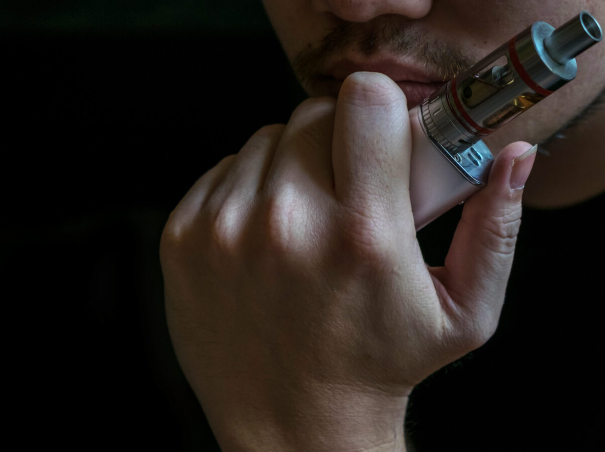 Man with concealed identity smoking a controversial vaping an electronic cigarette. Vaping is debatable in the health community if it is safe or a health risk