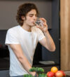 Handsome guy stay on modern kitchen, drinking glass of water in the morning time.